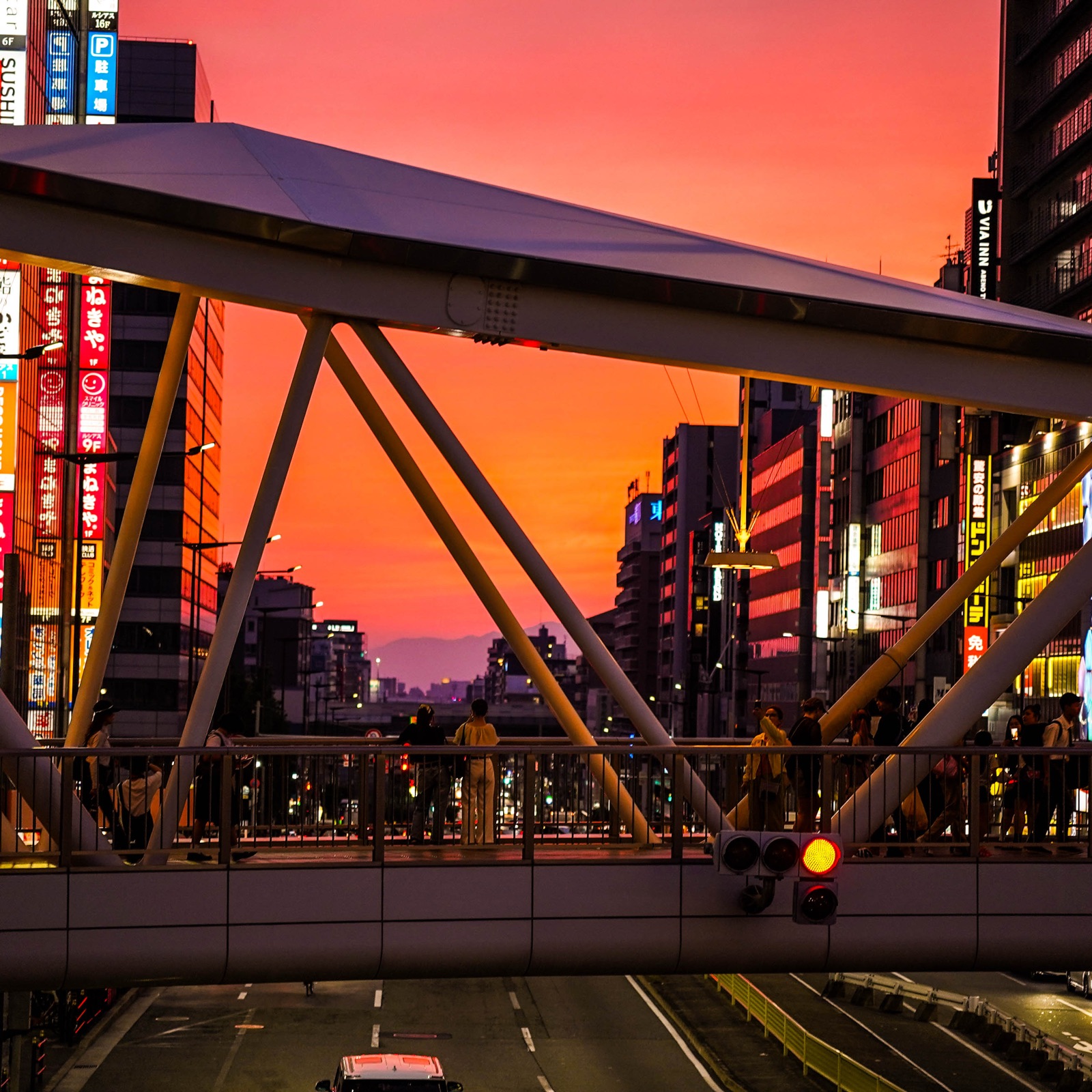 Pedestrians cross a steel walkway beneath a pink evening sky.