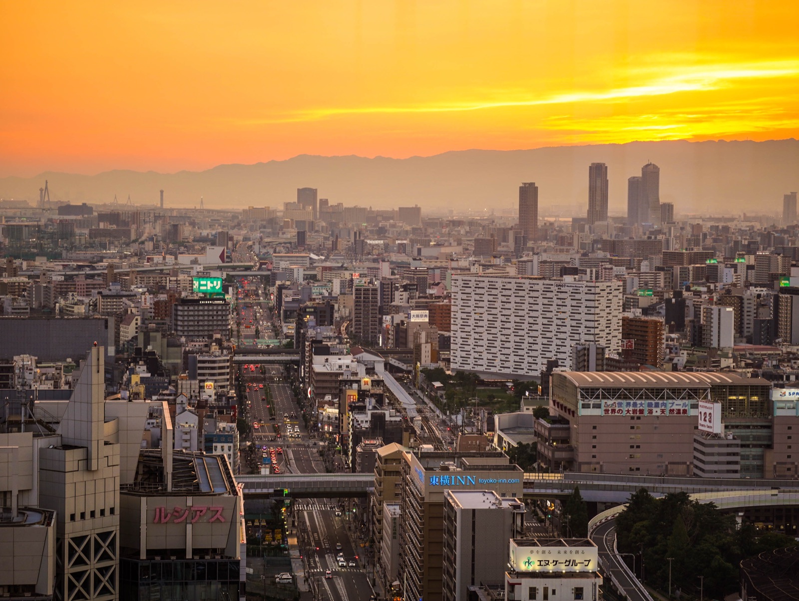 A wide city skyline glows beneath an orange sunset.