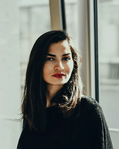 A woman in a dark sweater beside a bright window.