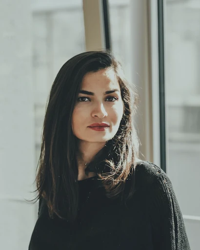 A woman in a dark sweater beside a bright window.