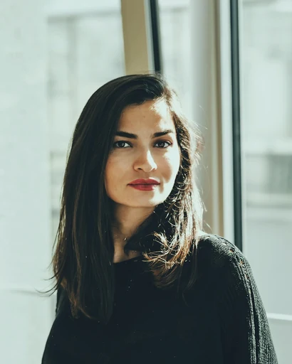 A woman in a dark sweater beside a bright window.