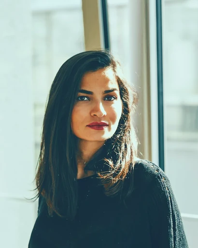A woman in a dark sweater beside a bright window.