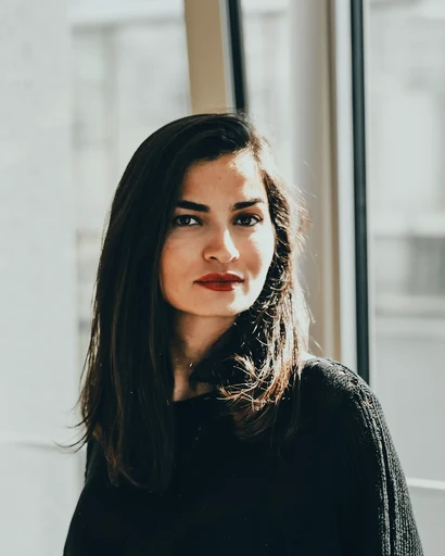 A woman in a dark sweater beside a bright window.