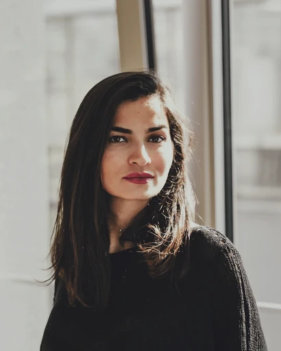 A woman in a dark sweater beside a bright window.