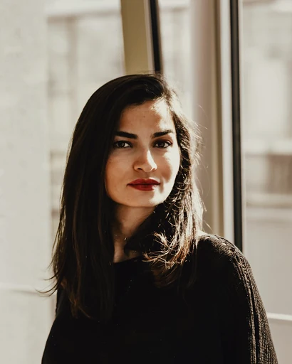 A woman in a dark sweater beside a bright window.