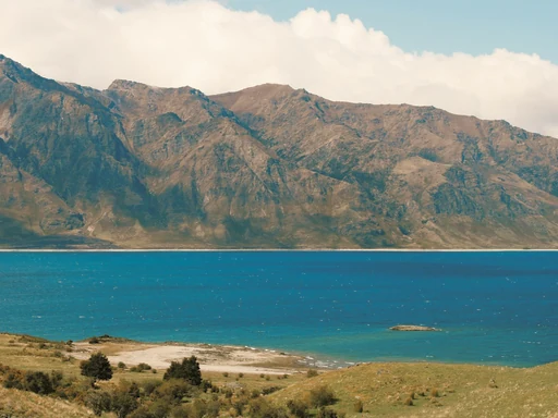Turquoise water and a rocky shore below rugged mountains.