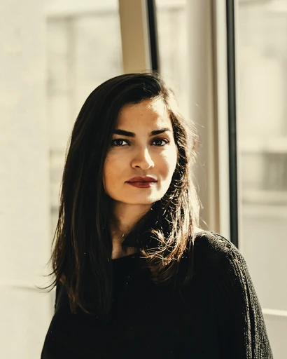A woman in a dark sweater beside a bright window.