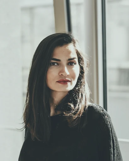 A woman in a dark sweater beside a bright window.