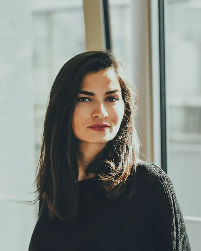 A woman in a dark sweater beside a bright window.